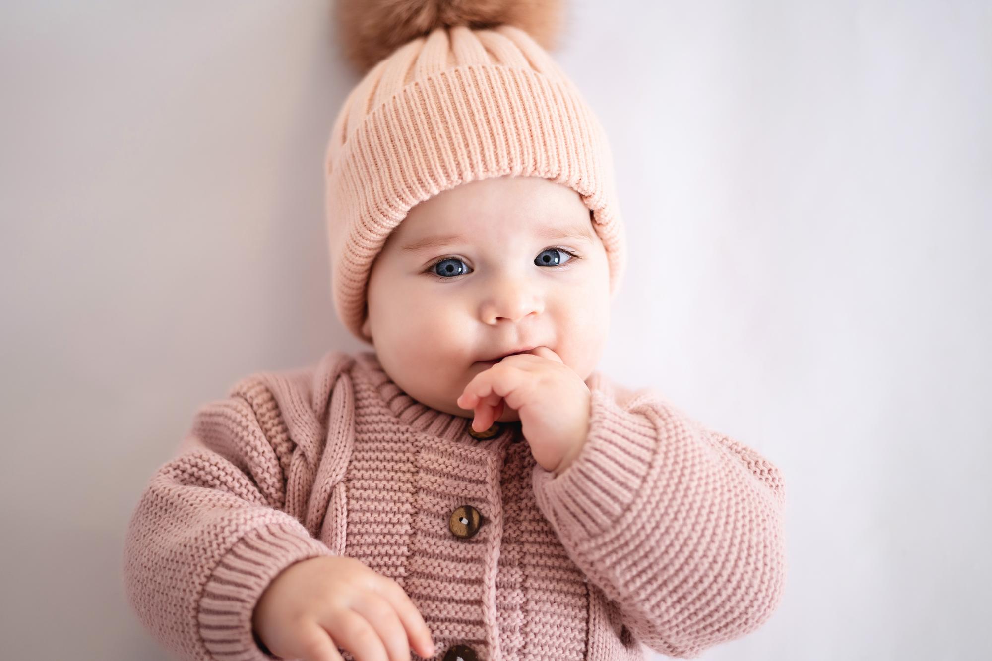 cute-little-girl-child-with-blue-eyes-pink-knitted-jumpsuit-hat-is-lying-her-back-looking-camera-white-background-isolated_515682-2692